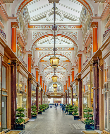 Old Bond Street, Mayfair, London, England, UK - Shoppers walking through the Royal Arcade. It is a historic Victorian shopping arcade that runs between Albermarle Street and Old Bond Street in the prosperous district of Mayfair. It has a saddled glass roof, richly decorated stucco arches, curved glass shop fronts and Ionic columns.