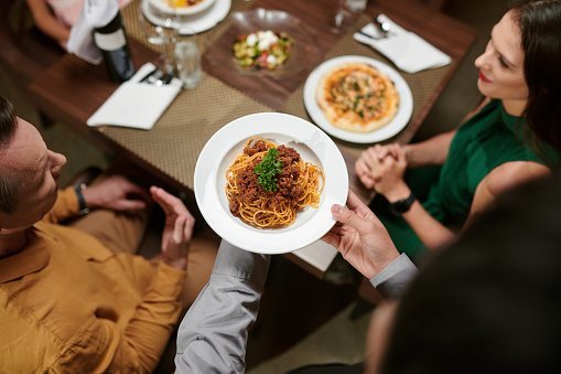 Restaurant waiter bringing plate with spaghetti bolognese to table