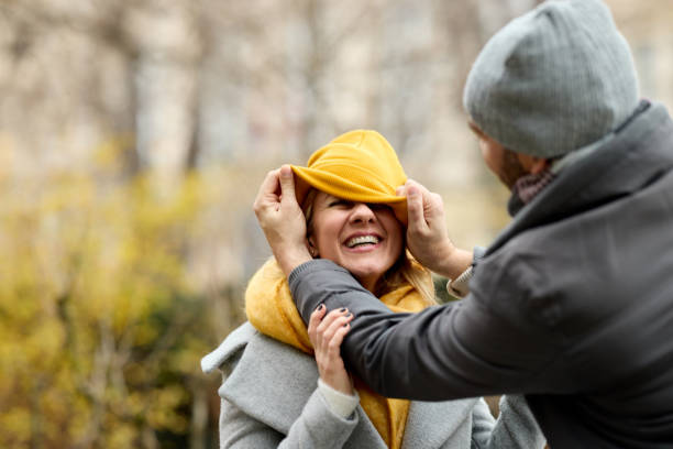 coppia di metà adulti affettuosa che si diverte molto nel parco - fun knit hat adult dating foto e immagini stock