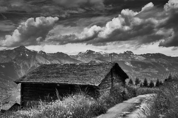 In the background there is a mountain range, and on the left a forest. There are footprints in the snow in front of the hut