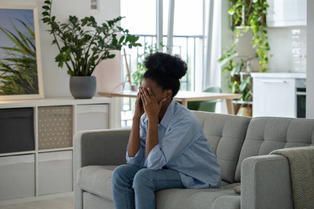 une femme afro-américaine opprimée et déprimée est assise sur un canapé avec des problèmes psychologiques et du stress - disgust women african ethnicity human face photos et images de collection