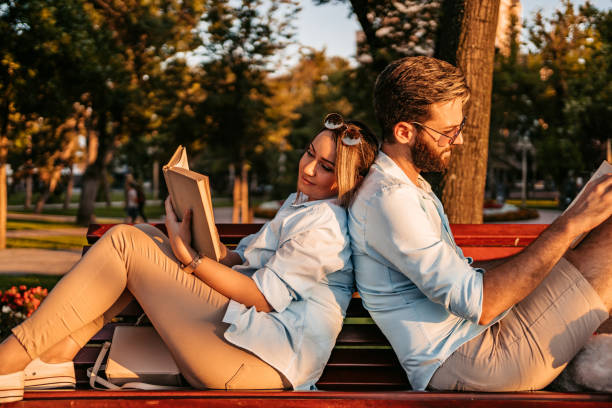 istock Young Couple Reading While Sitting On The Park Bench 1469189794