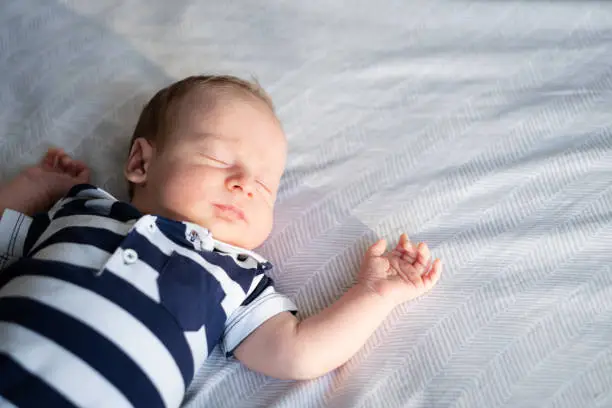 Photo of Little newborn caucasian brunet baby lying on back on bed wearing striped T-shirt sleeping.Half body shot, copy space