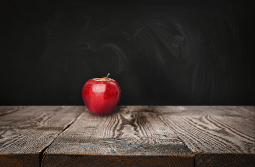 Fresh ripe red apple on wooden table near black chalkboard, space for text