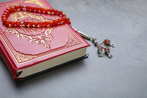 Muslim prayer beads and Quran on grey stone table, closeup. Space for text