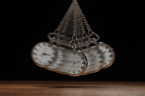 Hypnosis session. Vintage pocket watch with chain swinging over wooden surface on black background, motion effect