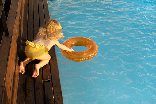 Cute pretty playful happy caucasian blonde two year old girl, child,kid, toddler having fun with water outdoor in summer, near swimming pool.Cheerful, careless childhood, leisure time lifestyle.