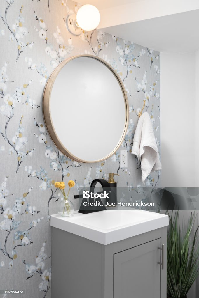 A bathroom with wallpaper and grey cabinet. Detail of a bathroom with a grey cabinet, wooden circular mirror, and patterned wallpaper. Bathroom Stock Photo
