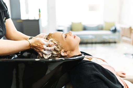 Beautiful smiling blonde woman receiving hair washing treatment in hair salon