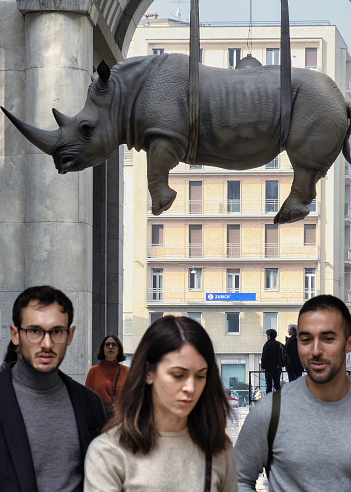 Brescia, Italy - October 16, 2022: A sculpture of a rhinoceros by Stefano Bombardieri hanging from the ceiling of a passageway in Brescia, Italy. In the foreground pedestrians.