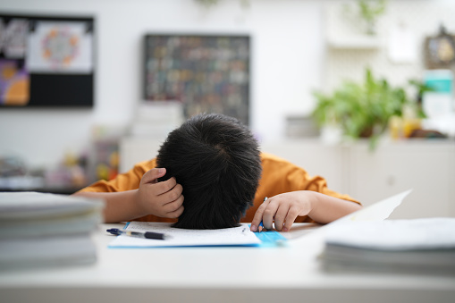 Young Asian boy is tired of doing homework, sitting at the table.