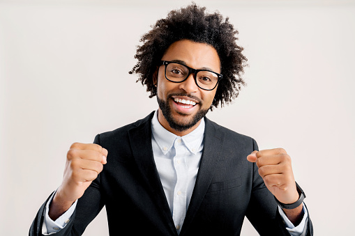 Extremely excited overjoyed african-american man with curly hair shouting making yes gesture, amazed with his victory, triumph, looking at camera and laughing, studio shot isolated on white background