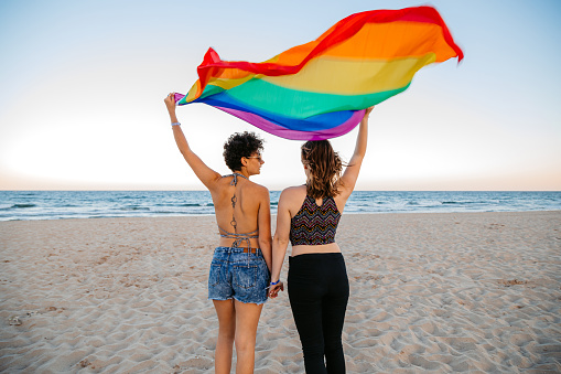 Beautiful young lesbian couple having fun on the beach in Albena, Bulgaria. Holding up a pride flag.