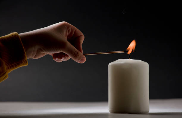 istock white candle with flame, little child hand with fire stick, black background 1469200910