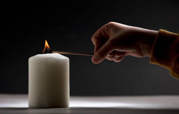 istock white candle with flame, little child hand with fire stick, black background 1469200914
