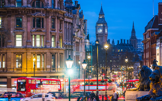 The iconic clocks of Big Ben overlooking Whitehall and the Landseer’s Lions of Nelson’s Column in Trafalgar Square in the heart of London illuminated at night.