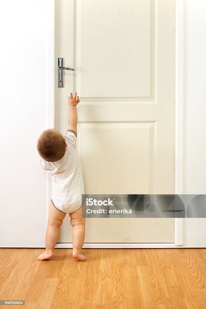 Baby boy in front of door Baby boy in front of a closed door, trying to reach the handle Baby - Human Age Stock Photo