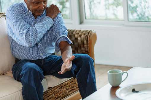 A senior African-American man sitting at home on a couch, rubbing his sore shoulder. It is painful from arthritis or an injury.