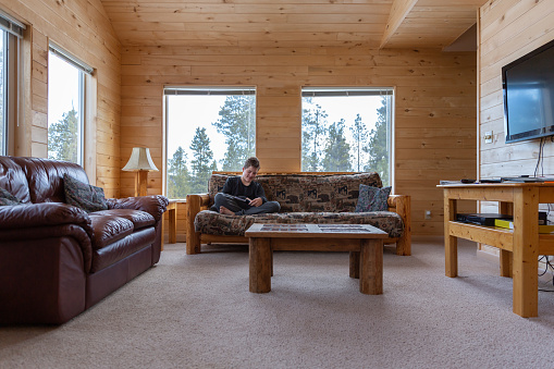 Teenage boy reading a magazine on a couch at a cabin in the Colorado mountains.