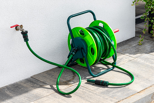 A garden hose connected to a faucet protruding from a building against a white facade.