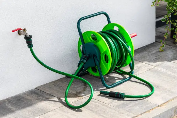 Photo of A garden hose connected to a faucet protruding from a building against a white facade.
