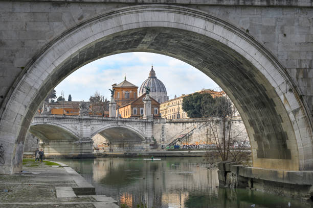 Rome, Lazio, Italy: Passing under the Umberto I Bridge, the Castel Sant'Angelo Bridge and the Vatican can be glimpsed. A walk from Lungotevere Tor di Nona, between Ponte Umberto I and Ponte Sant'Angelo on the opposite side of the Tiber is Lungotevere Castello