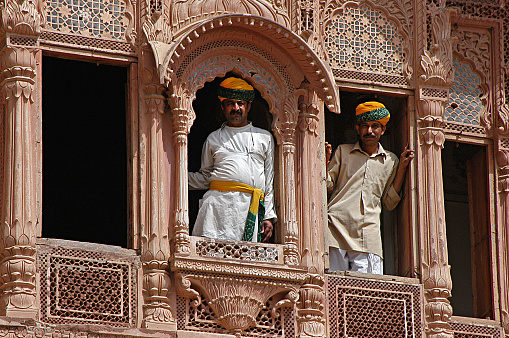 Rajasthan, India - March 14, 2006: Men leaning out of the decorated windows of a Haveli in the city of Jaisalmer