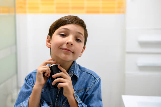 istock Smiling child sprays cologne on his neck while looking at the camera 1469214669