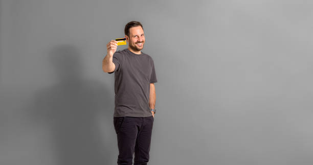 istock Smiling man showing credit card isolated on gray background 1469217524