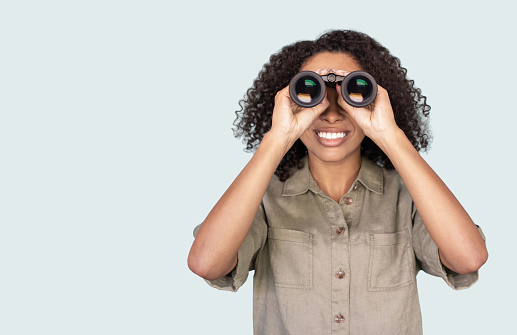 Excited smiling girl looking through binoculars, isolated on grey background