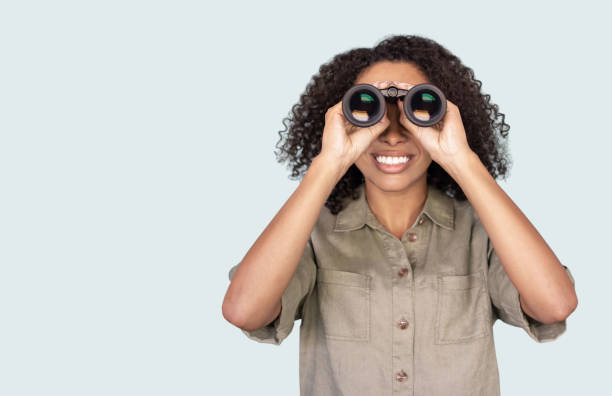 young woman looking through binoculars - olhando através imagens e fotografias de stock