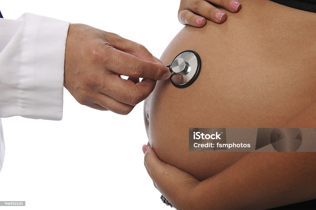A doctor is listening to unborn baby's heartbeat Pregnant woman being examine by a doctor with a stethoscope isolated on white Abdomen Stock Photo