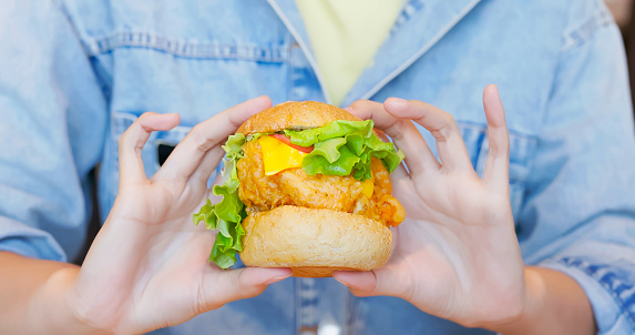 close up asian woman hand holding appetizing unhealthy fast junk food hamburger in food court or restaurant