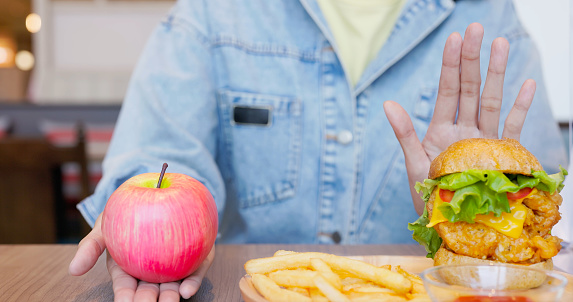 close up healthy eaing diet concept - asian woman hand hold apple choose eat apple refuse unhealthy junk food hamburger and fries combo