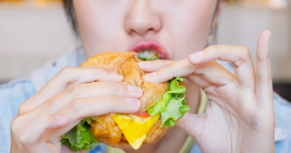 close up asian woman eating appetizing unhealthy fast junk food hamburger in food court or restaurant
