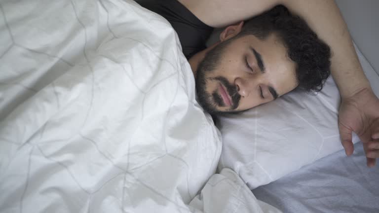 Young man sleeping in bed and looking for comfortable position