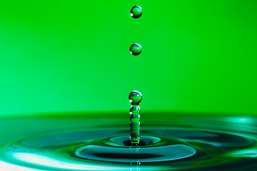 Close up macro color image depicting a water drop in a body of water with green background.
