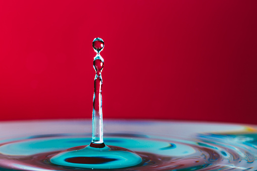Close up macro color image depicting a water drop in a body of water with red background.
