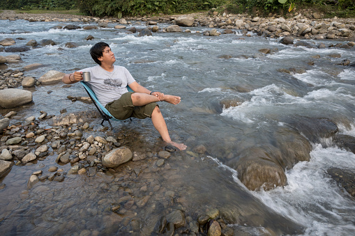 Men relaxing while enjoying coffee and playing cellphones in the river in the afternoon