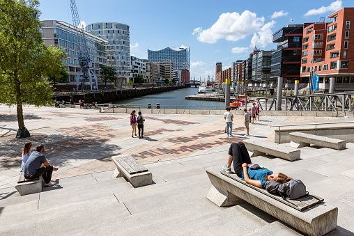 People lie and sit on the Magellan Terraces in the summer sun and look out over the Elbe philharmonic hall and Hamburg's Hafencity, Hamburg, Germany