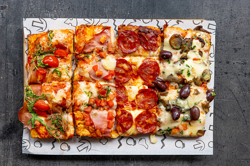 Pizza al taglio on restaurant table, rectangular slices with various toppings next to each other on a tray