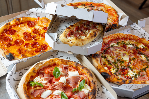 Pizza delivered in pizza boxes, several types of round baked pizza with various toppings