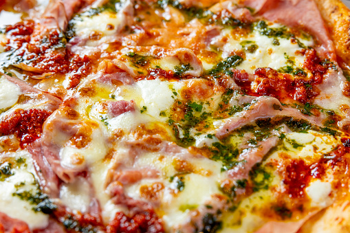 Close-up on baked Ham & Cheese pizza with mozzarella cheese and ham topping, seasoned with basil in olive oil, full frame