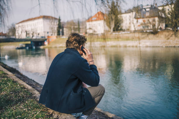 istock Young man siting and using a phone next to a river stock photo 1469232071