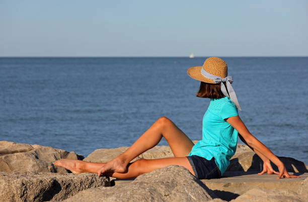 skinny girl in straw hat over the rocks by the sea in summer