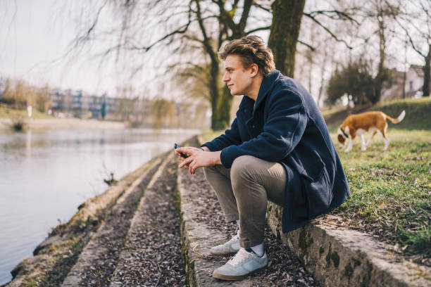 istock Young man siting and using a phone next to a river stock photo 1469232265