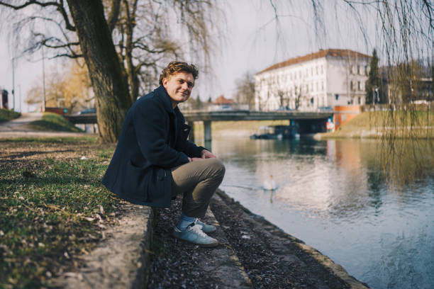 istock Young man siting and using a phone next to a river stock photo 1469232435