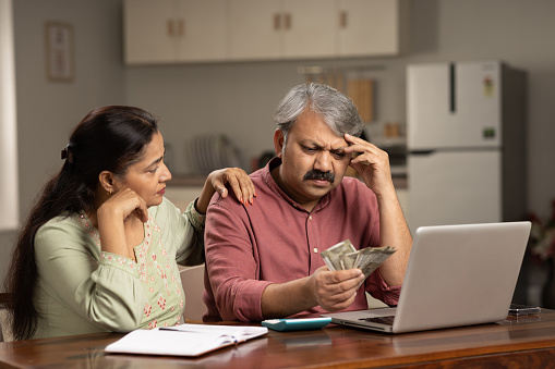 Worried mature couple counting money at white using laptop indoors