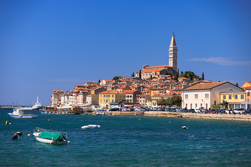 View on the town of Rovinj on the hill with Church of St. Euphemia tower on top across the blue sea with boats anchored
