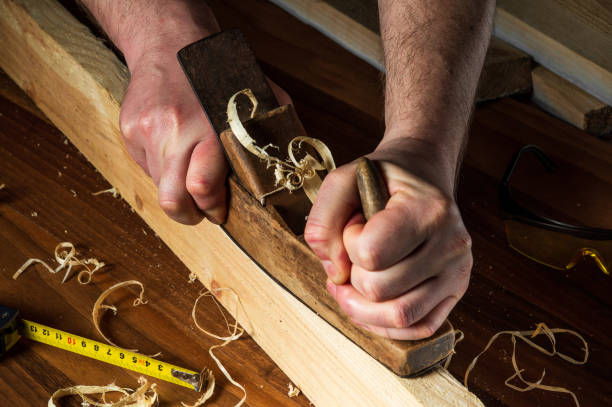 istock Woodworker using a hand plane to clean up a wooden board. Hands of the master closeup at work. Working environment in a carpentry workshop 1469236367